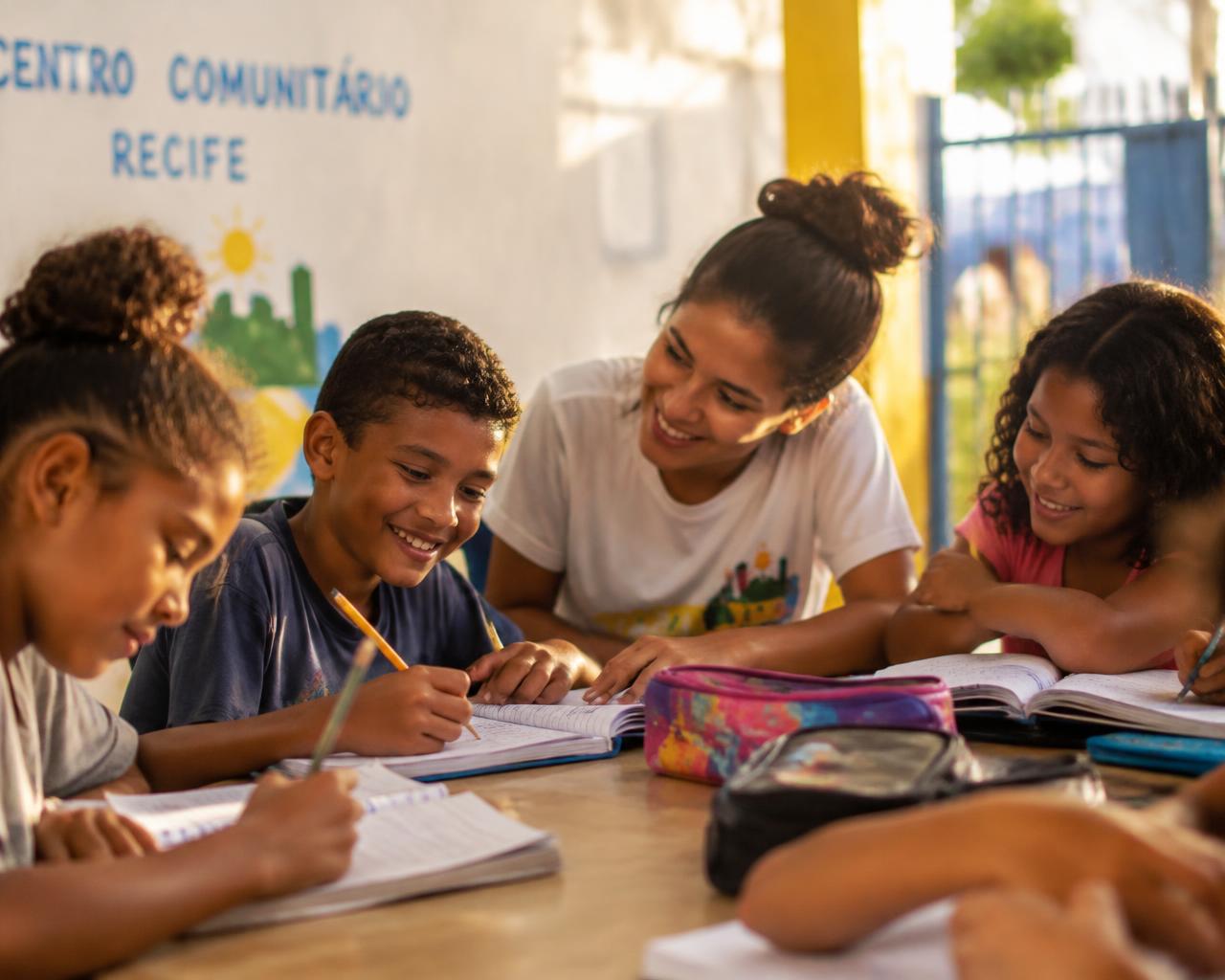 Crianças fazendo reforço escolar com uma voluntária no projeto